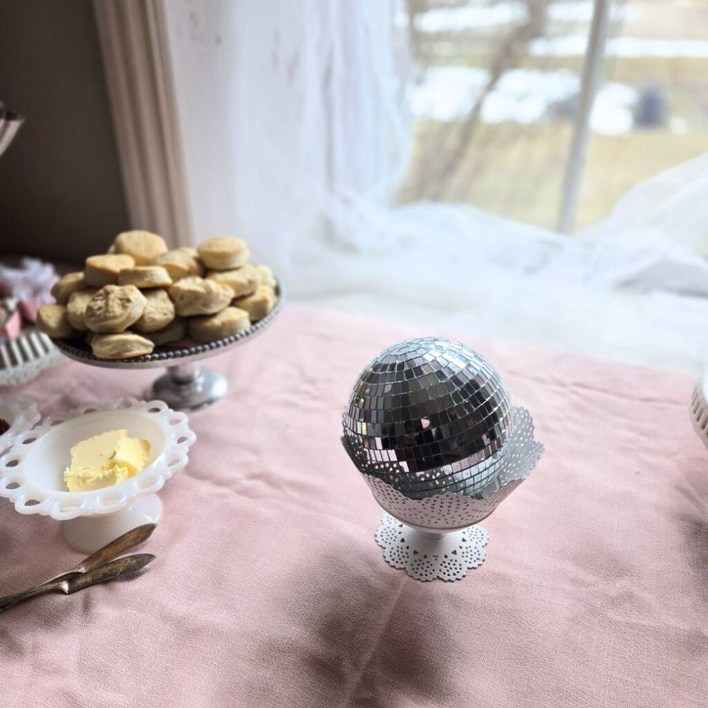 Small disco ball sitting in a bowl on a dessert table with a pink tablecloth.