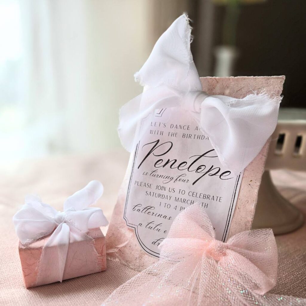 Pink invitation, favor box, and hairbow for a ballerinas and bows birthday party.