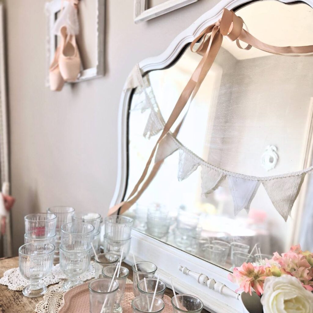 A dining room buffet decorated for a ballerina birthday party with pink ribbons, doilies, flowers, and glassware. 
