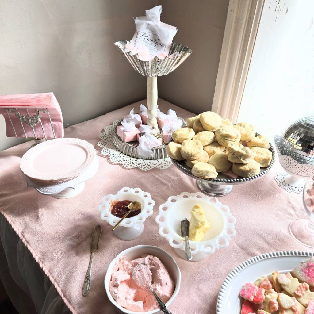 Dessert table with a pink tablecloth, white serving dishes and desserts.
