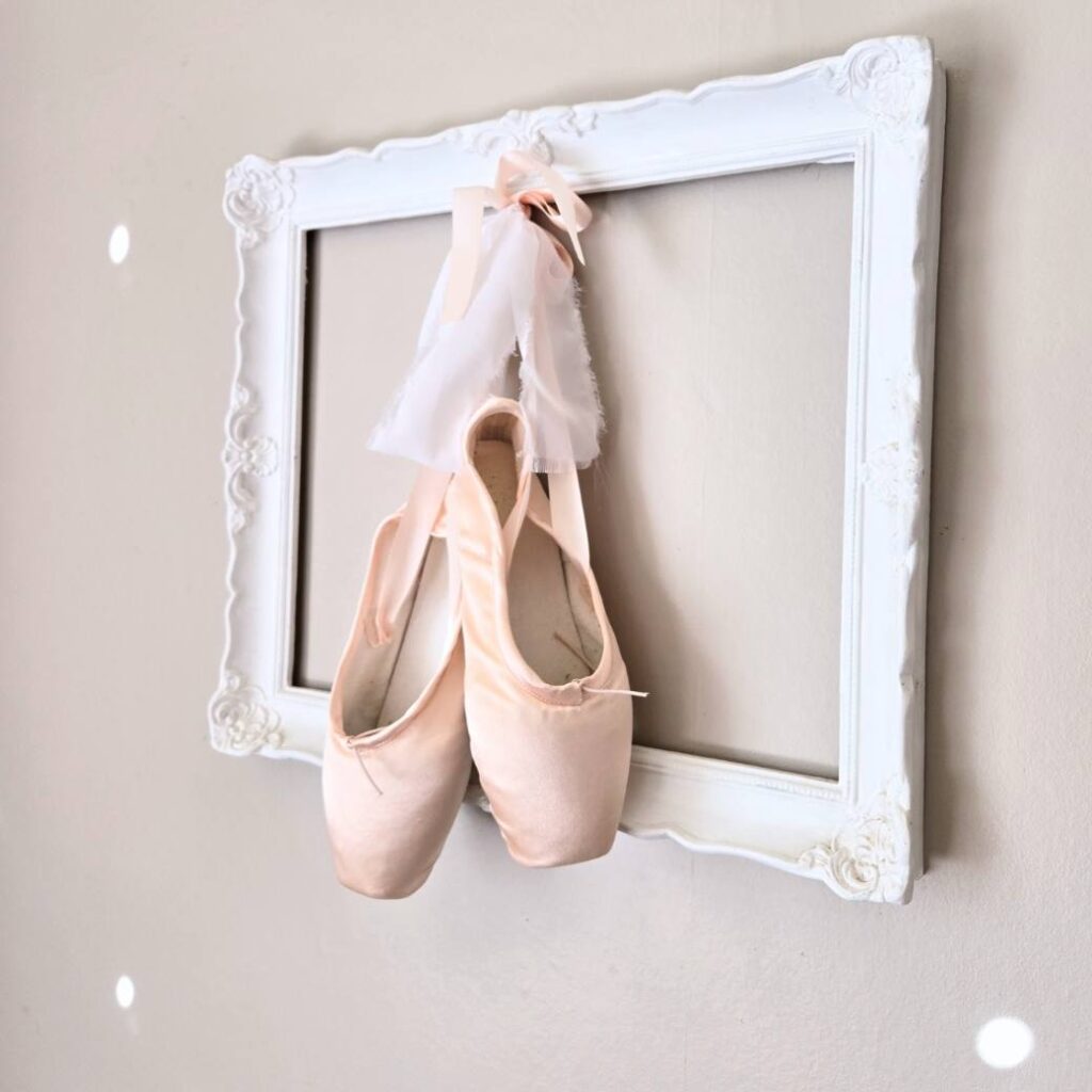 Pale pink point ballet shoes hanging in a frame on a wall.