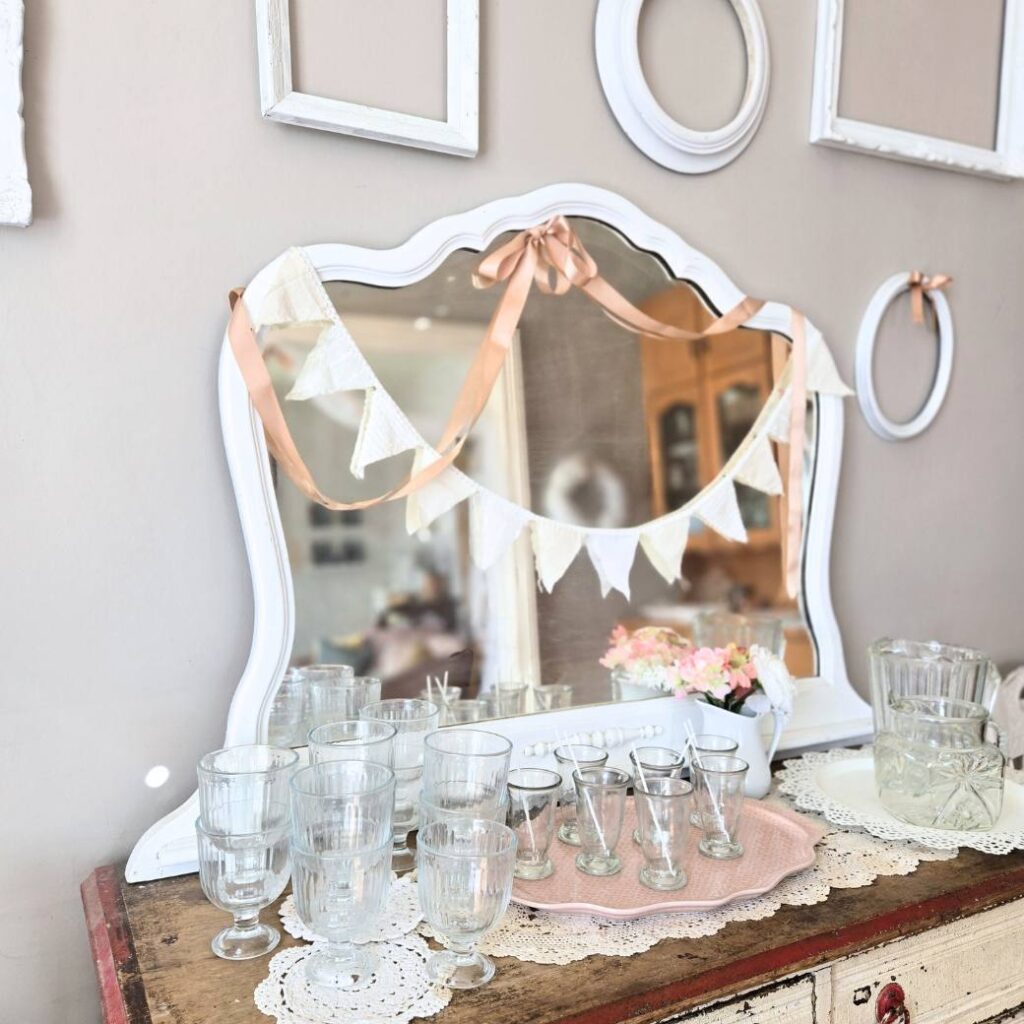 Antique buffet decorated with a pink bow and flowers and glassware.