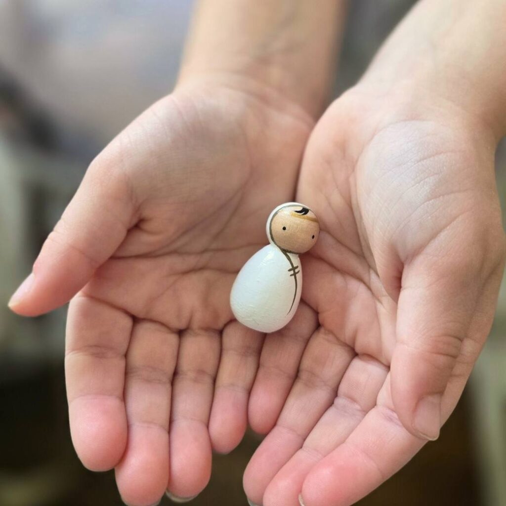 A child's hands holding a small peg doll painted as baby Jesus.