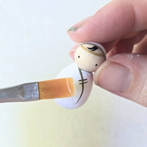 One baby peg doll being painted with clear sealer.