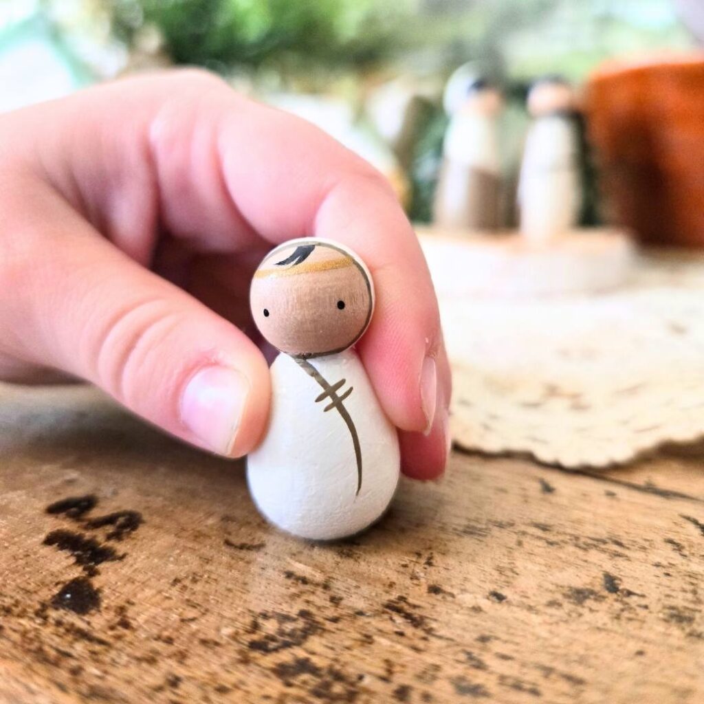 A peg doll baby Jesus held in a child's hand.