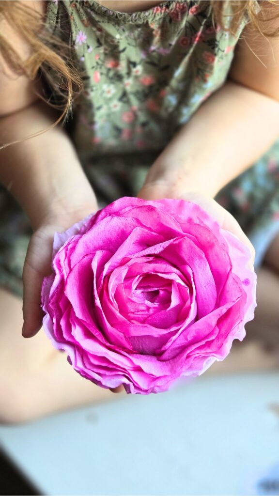 A pink handmade paper rose in a child's hands